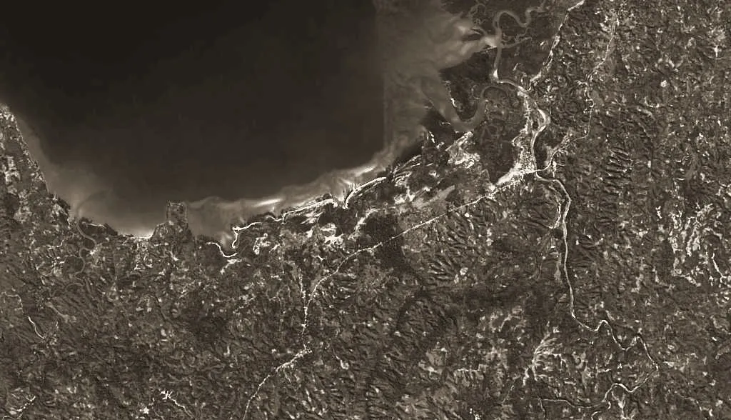 Vue satellite virée à l'encre : le fond d'une baie, un cordon de sable clair le long du rivage, un estuaire ramifié au nord-est, des rivières sinueuses et un couvert végétal continu ; aucune trame urbaine.