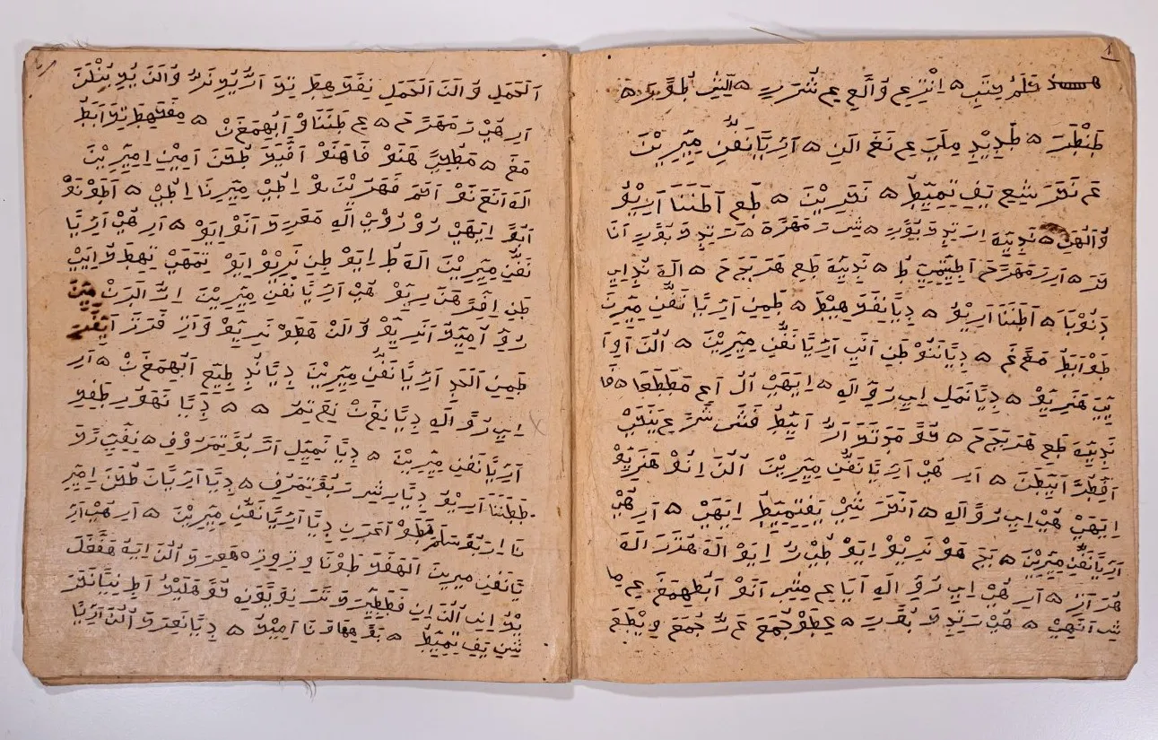 Manuscrit ouvert sur deux pages : un texte serré tracé à l'encre brune en caractères arabes, sur un papier épais et jauni aux bords effrangés, avec quelques taches.