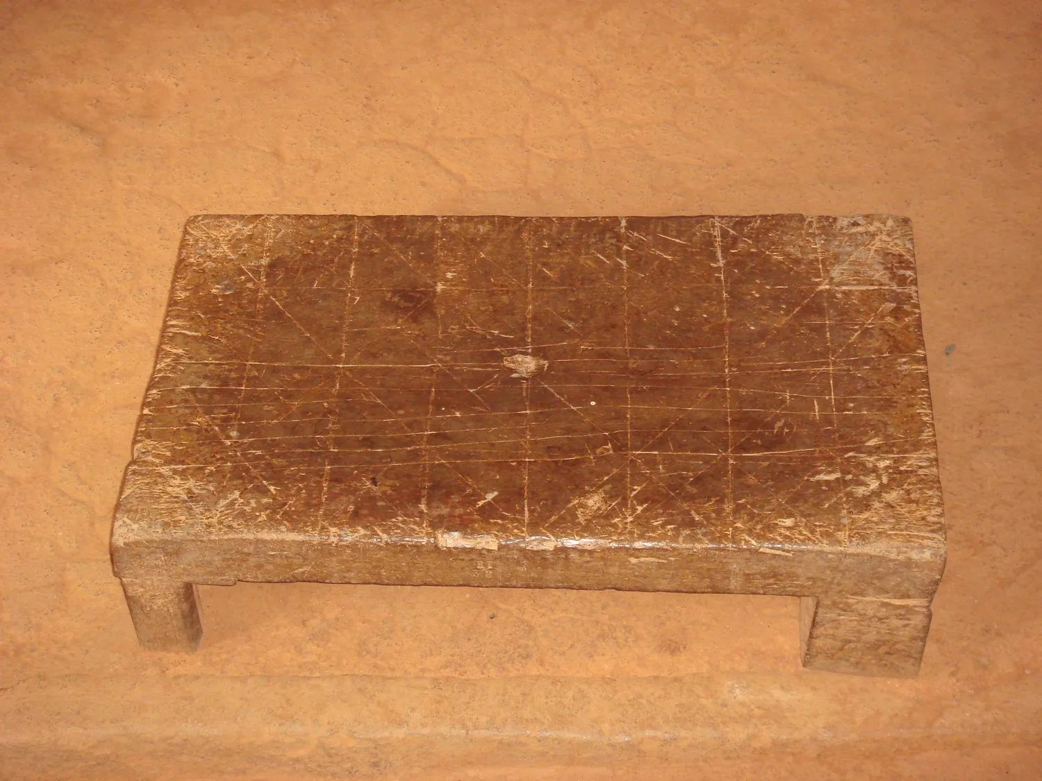 Un damier de fanorona gravé dans une dalle de pierre : deux rectangles emboîtés parcourus de lignes droites et de diagonales, la surface usée et lichénisée.